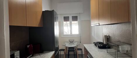 A compact kitchen with wooden cabinets, a marble countertop, and a central island with stools.