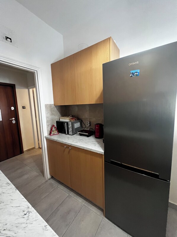 A kitchen with wooden cabinets, a stainless steel refrigerator, a microwave, and a coffee maker on the countertop. - Pnyka Apartment 3 (Athens)