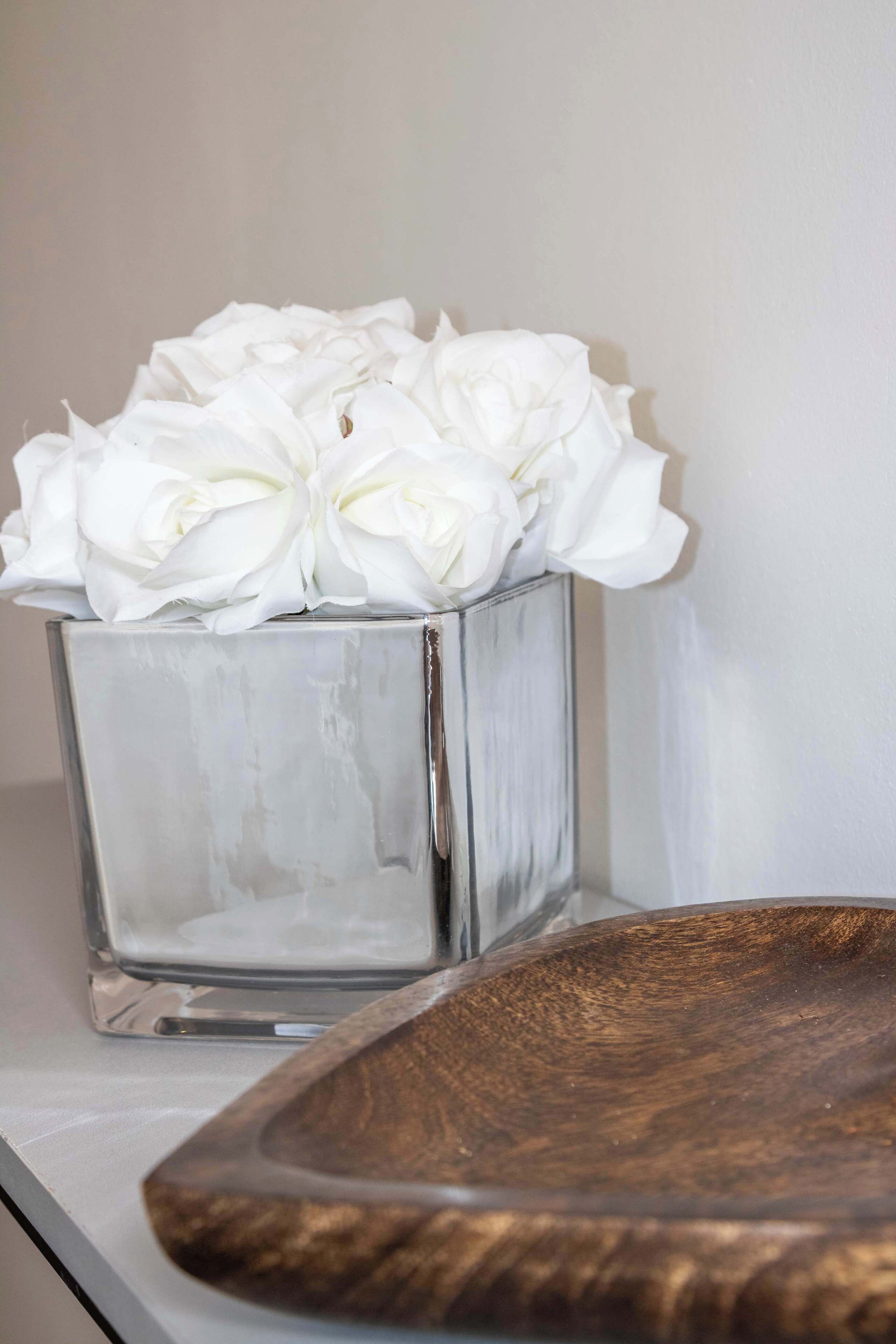 A clear glass vase with white flowers on a white surface.