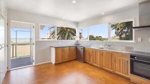 A spacious kitchen with wooden cabinets, a built-in oven, and large windows offering views of palm trees and a beach.