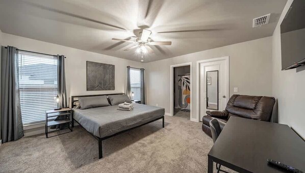 Une chambre à coucher comprenant un lit, un bureau, une chaise, un ventilateur de plafond et une armoire.