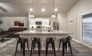 Une cuisine moderne dotée d’un îlot central, de tabourets de bar et de luminaires suspendus.