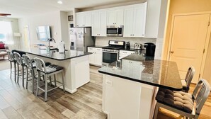 A modern kitchen with white cabinets, a central island, and a dining area with bar stools. - Beautiful townhome with community pool, shuttle to Bethany, and more! (Millville)