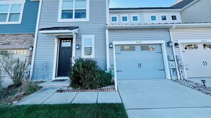 A two-story house with a dark front door, a garage, and a small front yard with a bush. - Beautiful townhome with community pool, shuttle to Bethany, and more! (Millville)