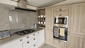 A modern kitchen with white cabinets, a gas stove, a microwave, and a built-in oven. - Daisy, A Hot Tub Home, Also Dog Friendly (Hoburne Holiday Park)