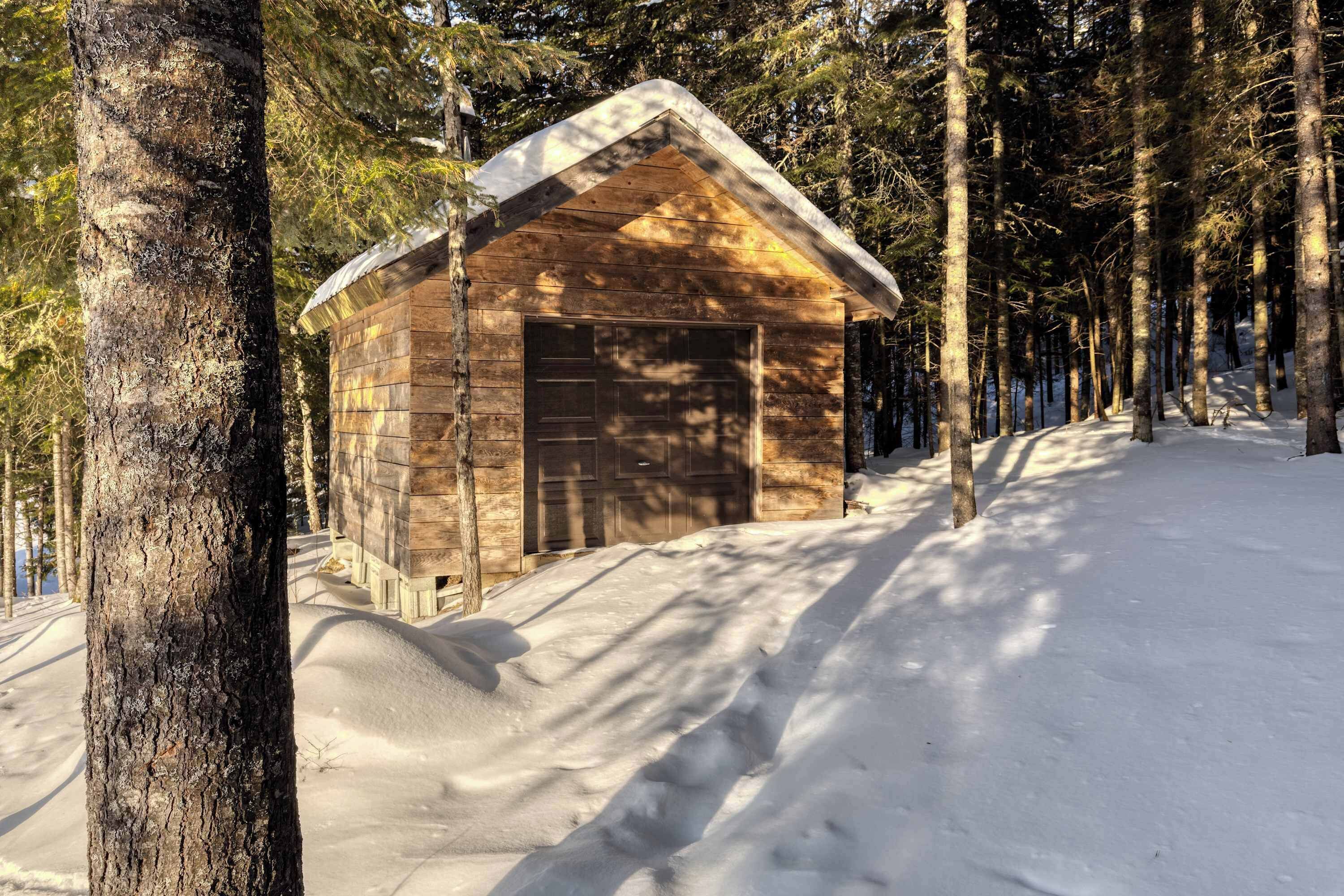 Una cabaña de madera con techo a dos aguas, rodeada de árboles altos y cubierta de nieve.
