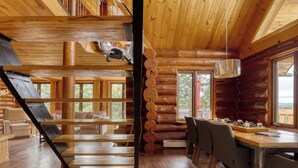 A log cabin interior with a wooden staircase, a dining area, and a view through large windows. - Spa and Great Comfort | Le Bo Bois Rond (Saint-Michel-des-Saints)