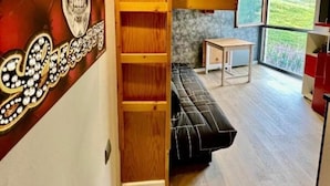 A modern interior with a wooden bookshelf, a black sofa, and a large window offering a view of the outdoors. - Orcieres - Studio at the foot of the slopes (Orcières)
