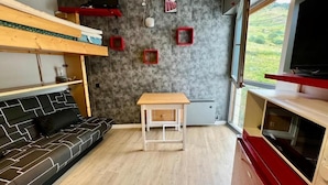 A compact living space with a sofa, a small table, a TV, and a window with a view of greenery. - Orcieres - Studio at the foot of the slopes (Orcières)