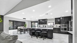 A modern kitchen with dark cabinets, a central island with bar stools, and stainless steel appliances. - Luxury 6BR Vegas Villa w Pool &Spa, Near The Strip (Las Vegas)
