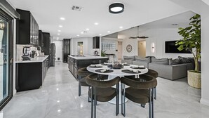 A modern kitchen with dark cabinets, a central island, and a dining area with a round table and chairs. - Luxury 6BR Vegas Villa w Pool &Spa, Near The Strip (Las Vegas)