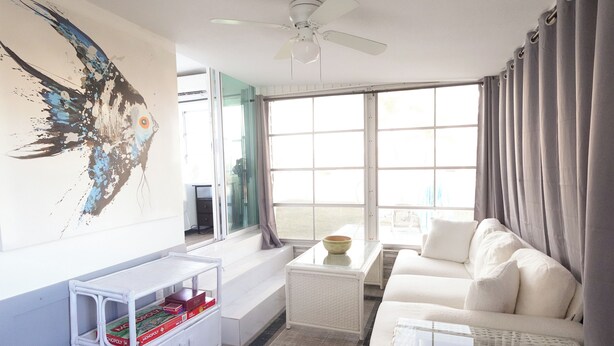 A modern living room with a white sofa, a glass coffee table, and a white side table with a Monopoly game.