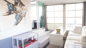 A modern living room with a white sofa, a glass coffee table, and a bookshelf with board games.