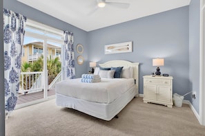 A bedroom with a bed, two bedside tables, a ceiling fan, and a view of the outside.