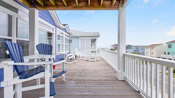 Une terrasse en bois avec des sièges extérieurs, un espace abrité et une vue sur les maisons voisines.