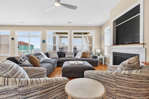 A living room with a gray sectional sofa, striped armchairs, a round coffee table, and a fireplace. - Ocean Isle Beach Gem: Steps to Beach & Pool! (Ocean Isle Beach)