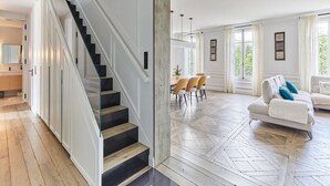 A spacious living area with a staircase, a dining area with chairs, and a sofa with cushions. - Incredible Apartment Etoile Porte Maillot (Paris)