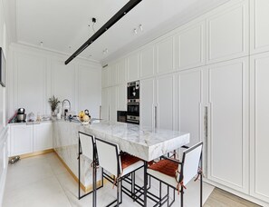 A modern kitchen with white cabinetry, a marble island, and a built-in oven.