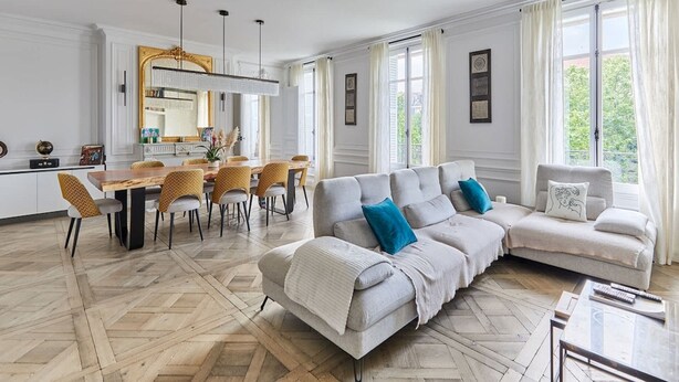 A spacious living room with a large sofa, a dining area with chairs, and a kitchen in the background. - Incredible Apartment Etoile Porte Maillot (Paris)