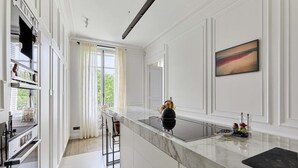 A modern kitchen with a marble countertop, a black kettle, and a painting on the wall. - Incredible Apartment Etoile Porte Maillot (Paris)