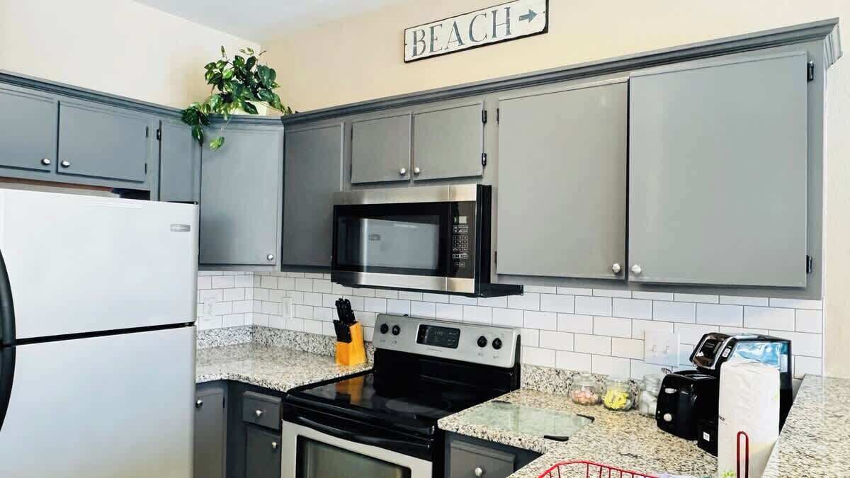 A kitchen with grey cabinets, a stainless steel refrigerator, a microwave, an oven, and a granite countertop.