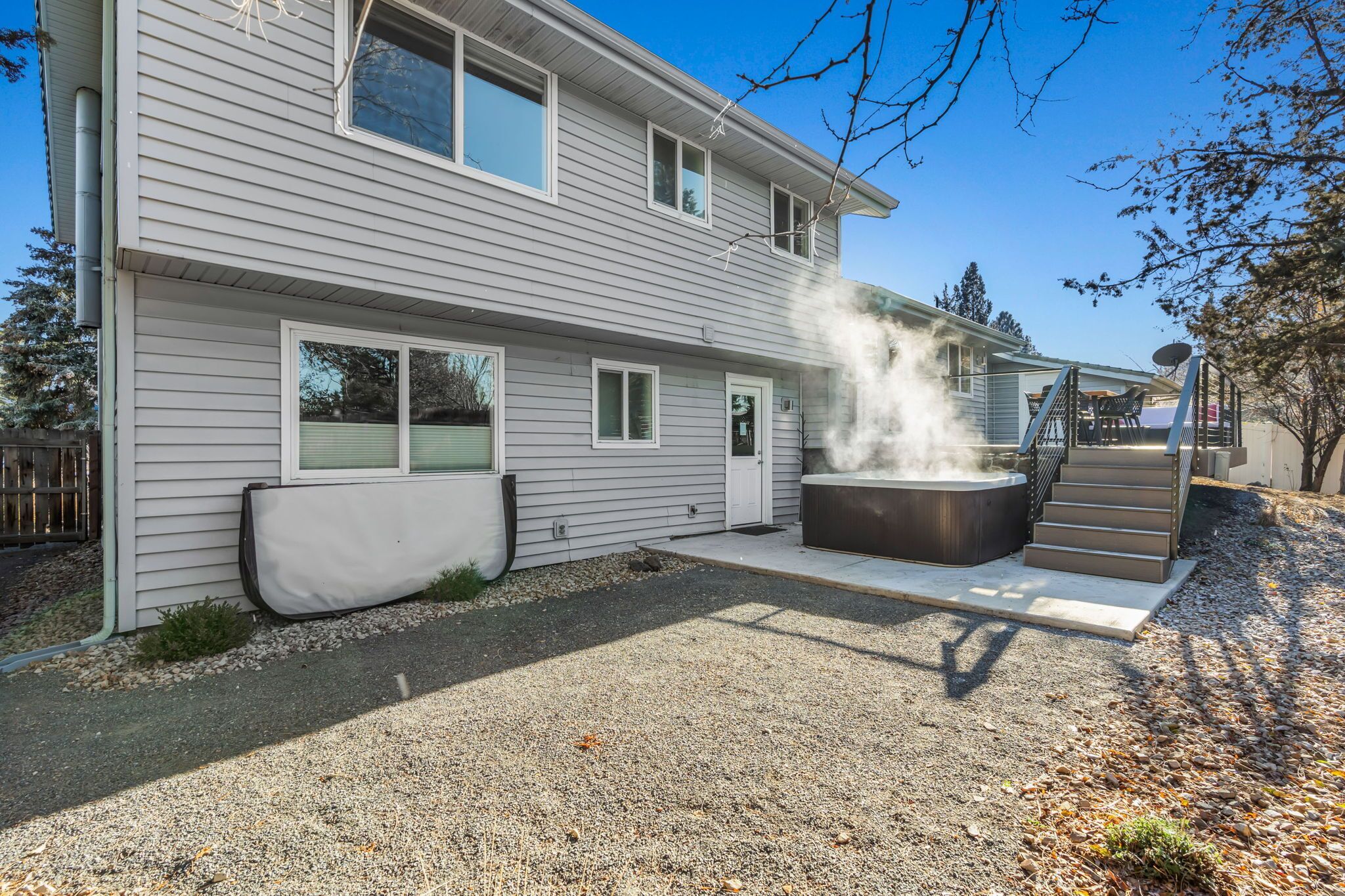 A two-story house with a covered patio area featuring a hot tub and a staircase leading to an upper level.