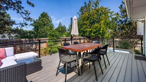 A deck with a table and chairs, a sofa, and a covered umbrella. - New! Hot Tub ~ Foosball ~ Bonus Room ~ Dog Friendly ~ AC! (Bend)