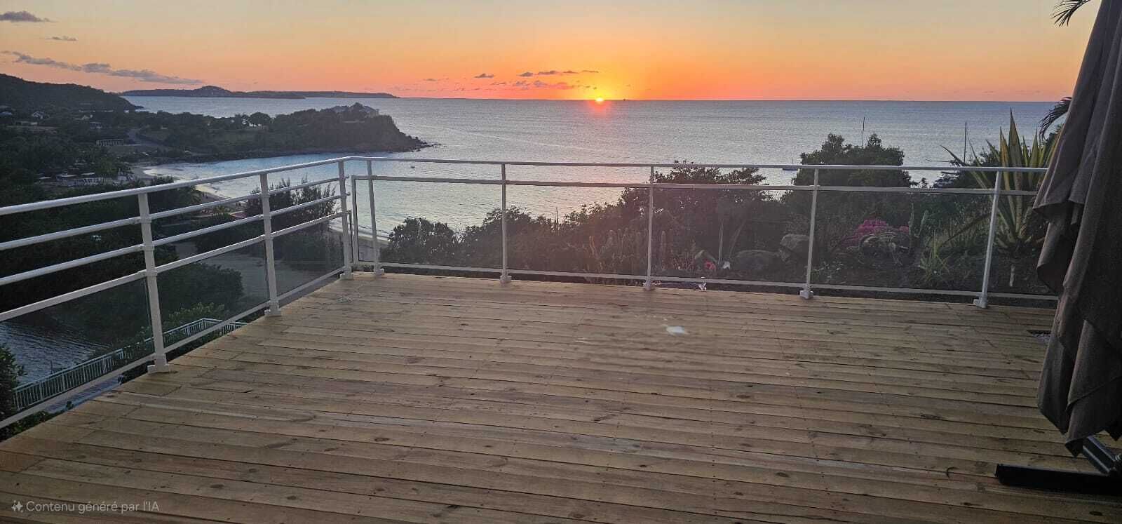 Eine Holzterrasse mit Metallgeländer, die Blick auf einen Sonnenuntergang über dem Meer bietet.