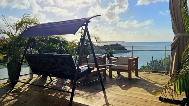 A wooden deck with a swing chair, a table, and an umbrella. - Sunset View (Saint Martin)