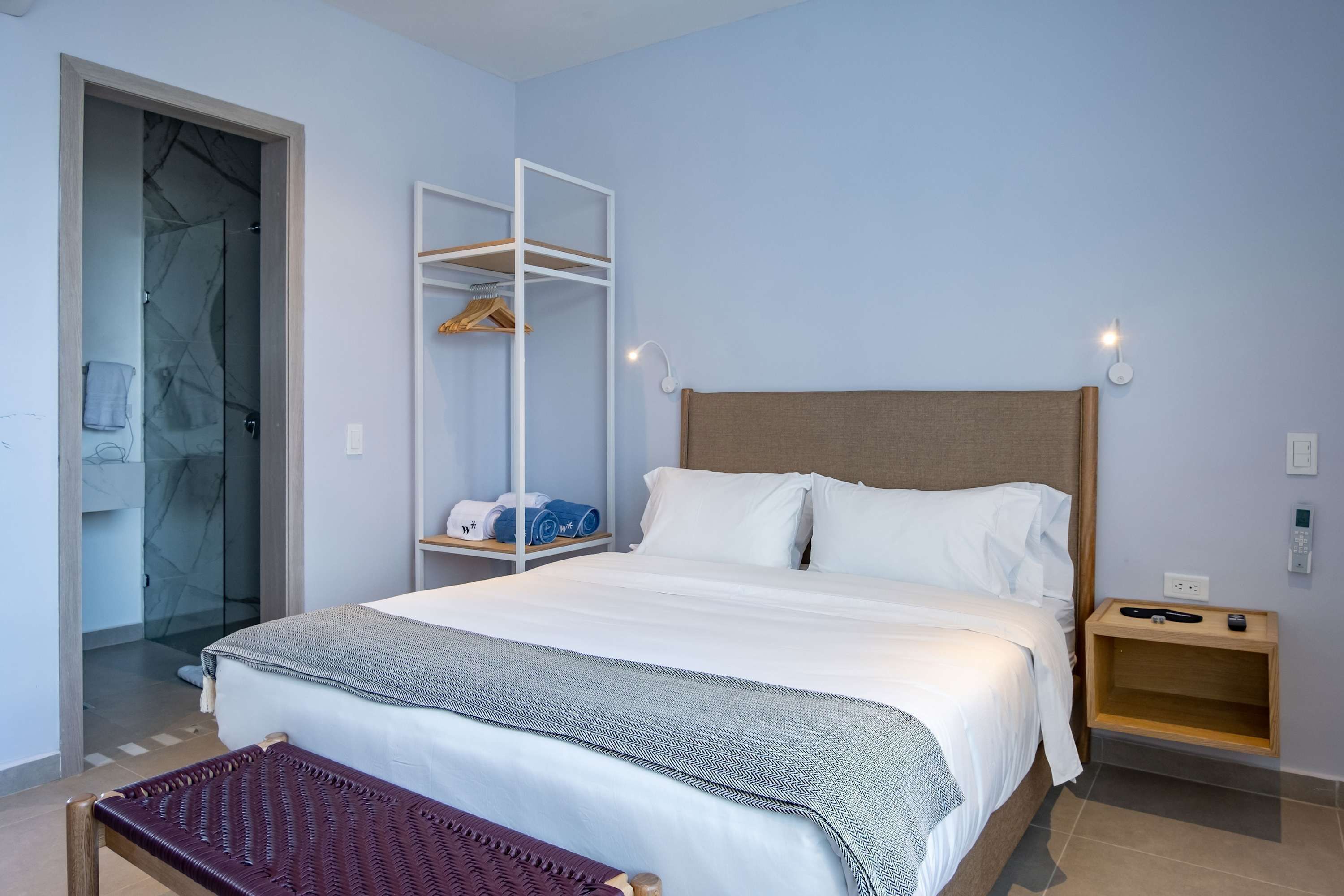 A neatly arranged hotel room with a bed, a bedside table, a wardrobe, and a bench.