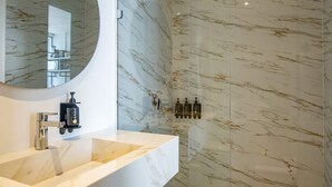 Un baño moderno con tocador de mármol, espejo redondo y zona de ducha con mampara de vidrio.