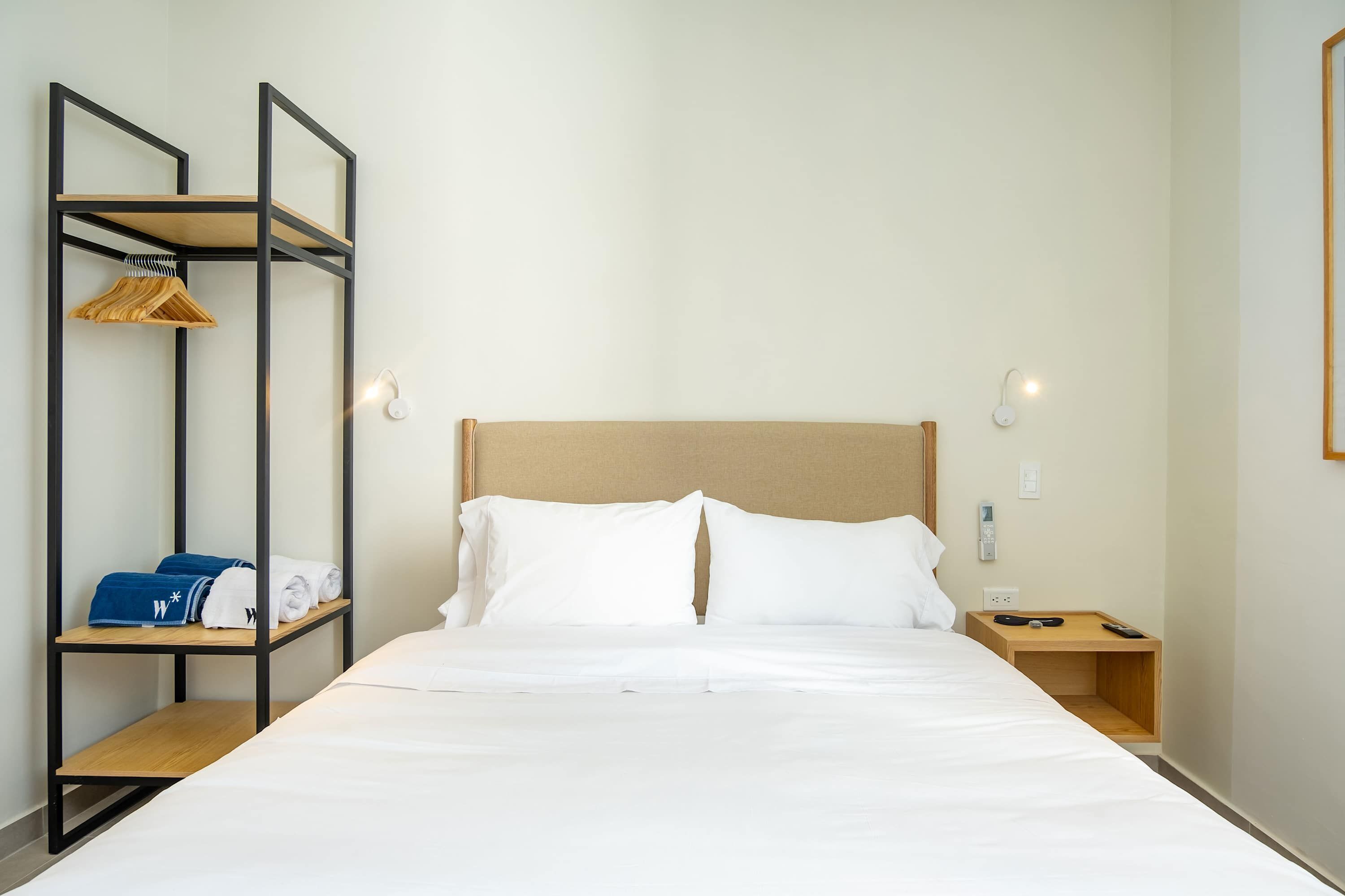A neatly made bed with white linens, a wooden headboard, and a small wooden nightstand with a remote control.