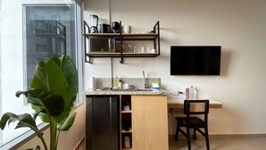 Una cocina compacta equipada con microondas, cafetera y refrigerador pequeño. Hay una zona de comedor con una silla y un televisor montado en la pared.