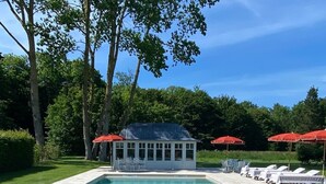 Una piscina rectangular con agua azul cristalina, rodeada por una solana con baldosas. Se observa una zona de estar cubierta con sombrillas rojas y sillas de descanso.