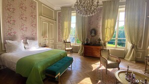Un dormitorio elegante con una cama grande, un banco, un aparador y una araña.