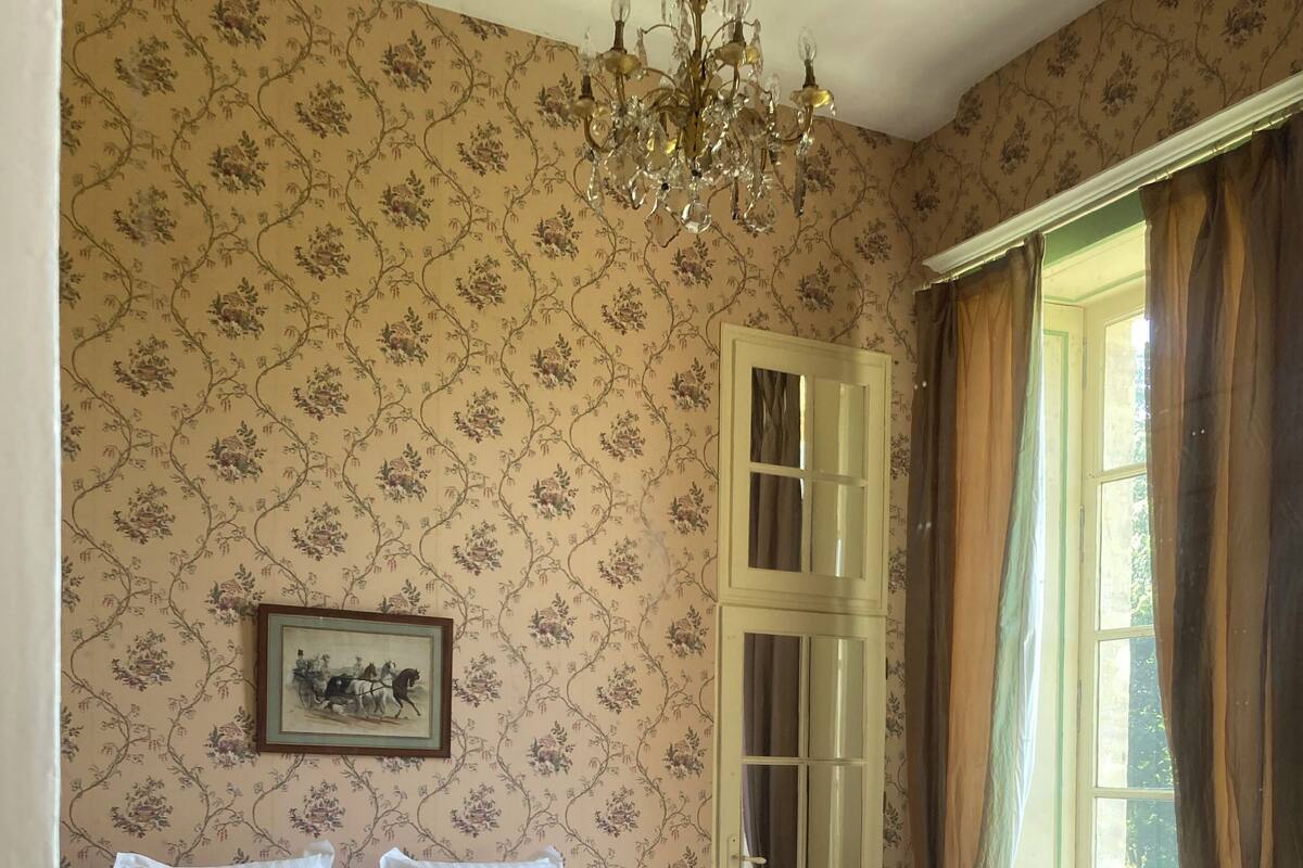 Una habitación con una cama, dos jarrones de latón, un candelabro, un cuadro enmarcado y una ventana con cortinas.