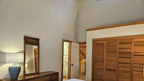 Een slaapkamer met een houten dressoir, een spiegel, een bed en een kledingkast.