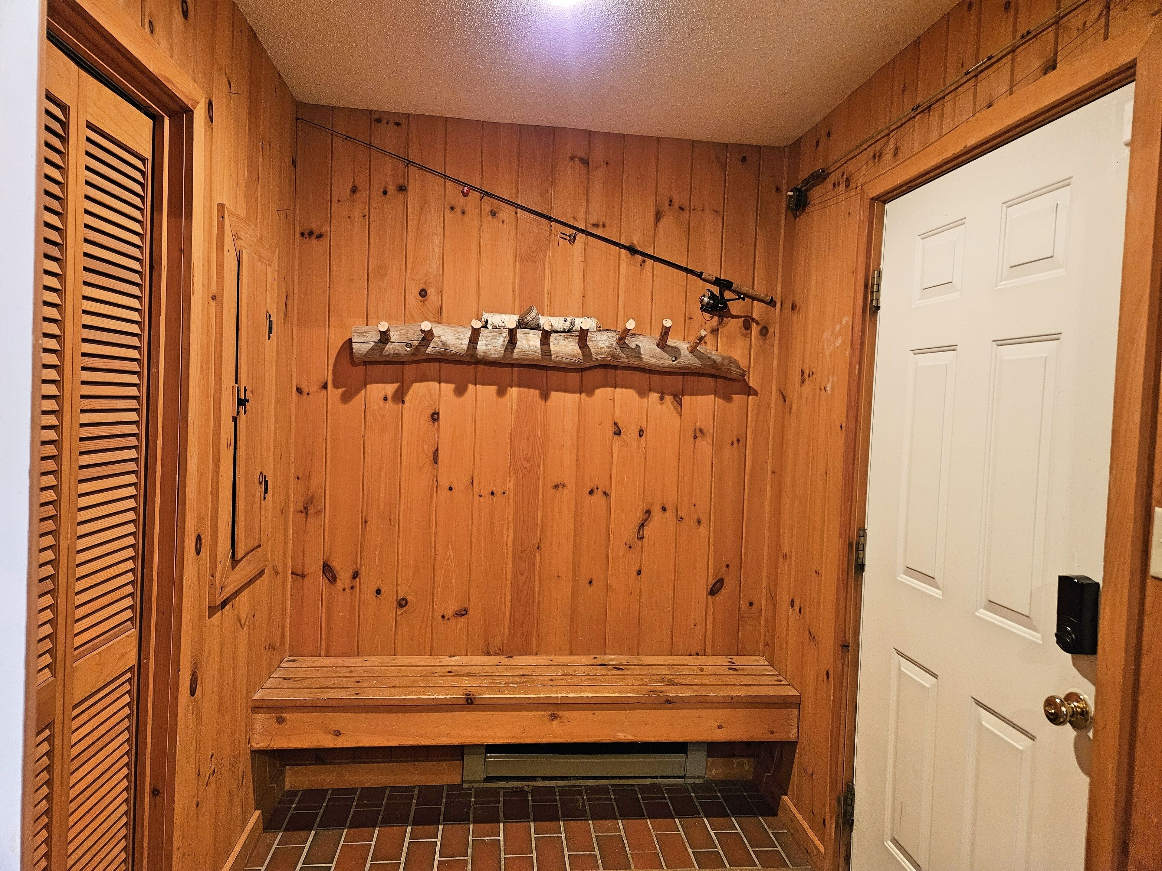 A wooden sauna room with a bench, a wooden shelf with logs, and a white door.