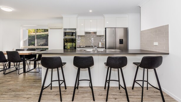 A modern kitchen with white cabinets, a stainless steel refrigerator, and a large island with bar stools. - Bayview • Pet-Friendly Beach House for 6 • Fenced Yard • Walk to Beach (Agnes Water)