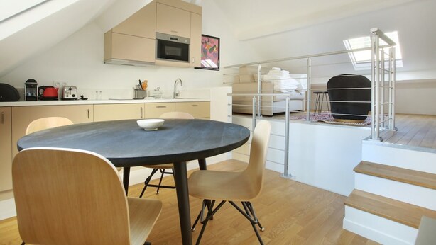 A modern kitchen with a dining area, wooden flooring, and a staircase leading to an upper level. - Sublime and new Triplex Le Marais/beaubourg (Paris)