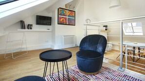 A modern loft apartment with a high ceiling, skylight, a black round table, a blue velvet chair, a colorful rug, and a dining area with a metal railing. - Sublime and new Triplex Le Marais/beaubourg (Paris)