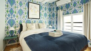 A bedroom with patterned wallpaper, a bed with a blue blanket, a framed artwork, and an air conditioning unit. - Sublime and new Triplex Le Marais/beaubourg (Paris)