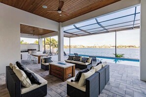 A modern outdoor living area with wicker furniture, a wooden coffee table, and a view of a body of water. - Skyline Paradise Retreat (Cape Coral)