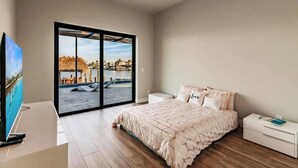 Quarto moderno com uma cama grande, ventilador de teto, TV e porta de vidro deslizante que dá para uma área de piscina.