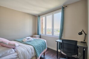 A bedroom with a bed, a desk, and a chair. There is a window with curtains, and a view of buildings outside. - Sublime 2 Bedroom Flat Quai de Seine Eiffel Tower (Paris)