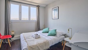 Ein Schlafzimmer mit einem Bett, einem Sessel, einem Schreibtisch und einem Fenster mit Vorhängen.