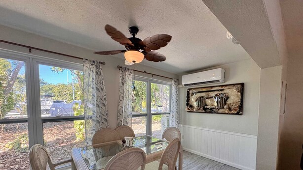 A dining area with a glass table and wicker chairs, large windows with curtains, a ceiling fan, and an air conditioning unit. - Villa Mars In Marathon (Marathon)