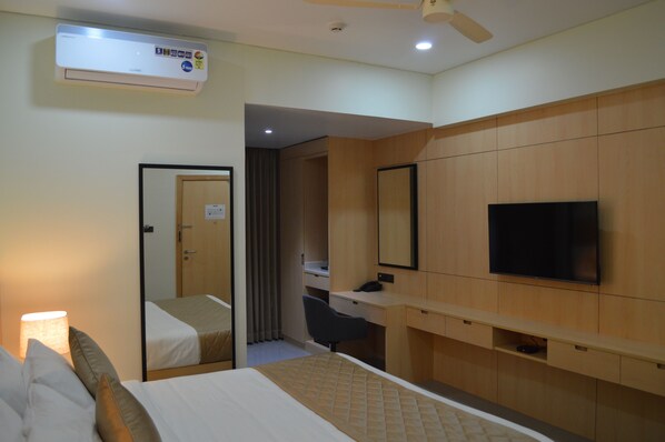 A hotel room with a bed, a desk, a chair, a television, and an air conditioning unit. - JBR Residency (Ramanathapuram)