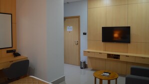 Een hotelkamer met een houten bureau, een aan de muur bevestigde televisie, een klein tafeltje met een afstandsbediening en een prullenbak.