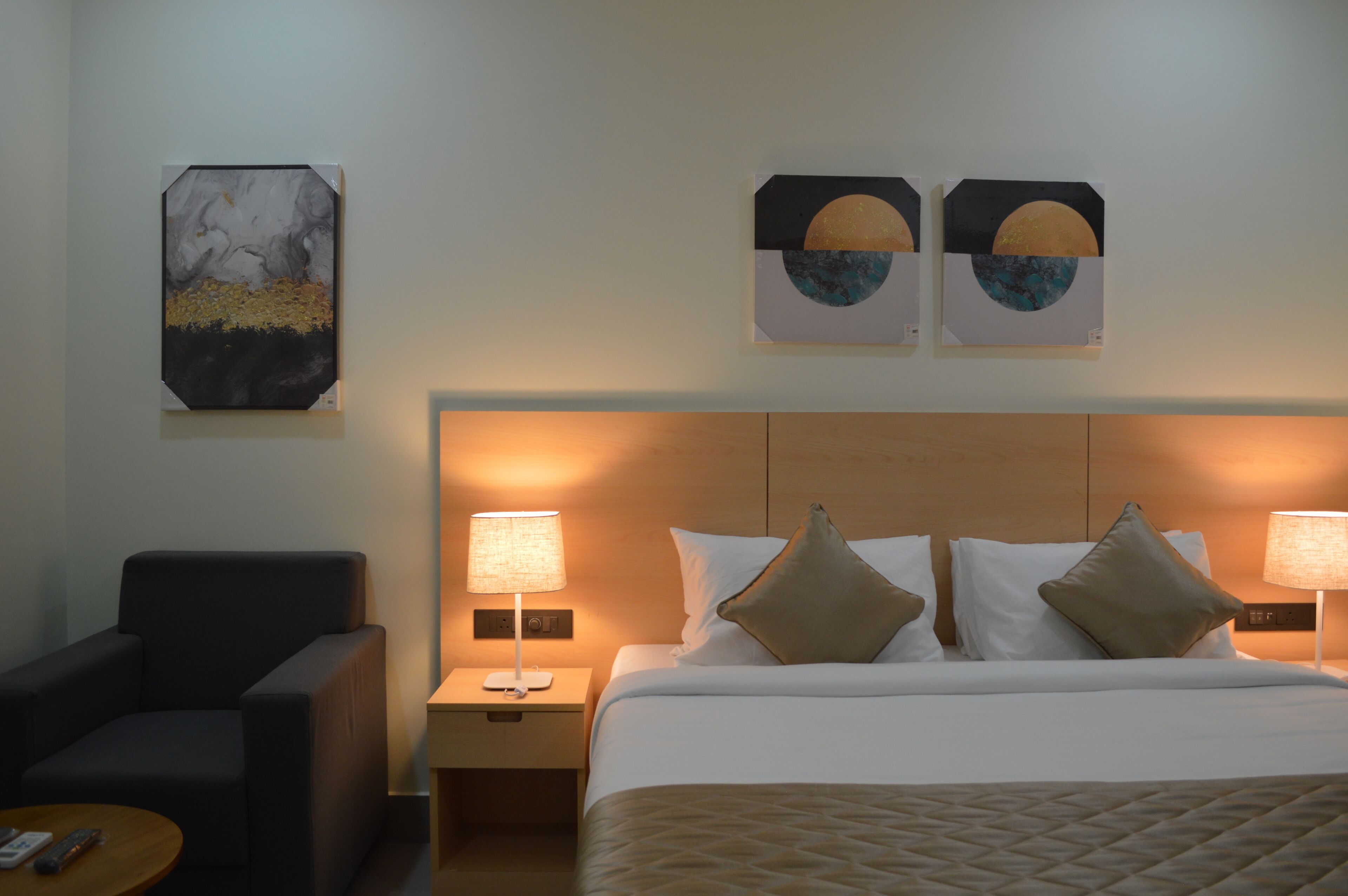 Una habitación de hotel con una cama, dos mesitas de noche con lámparas, una silla y una obra de arte en la pared.